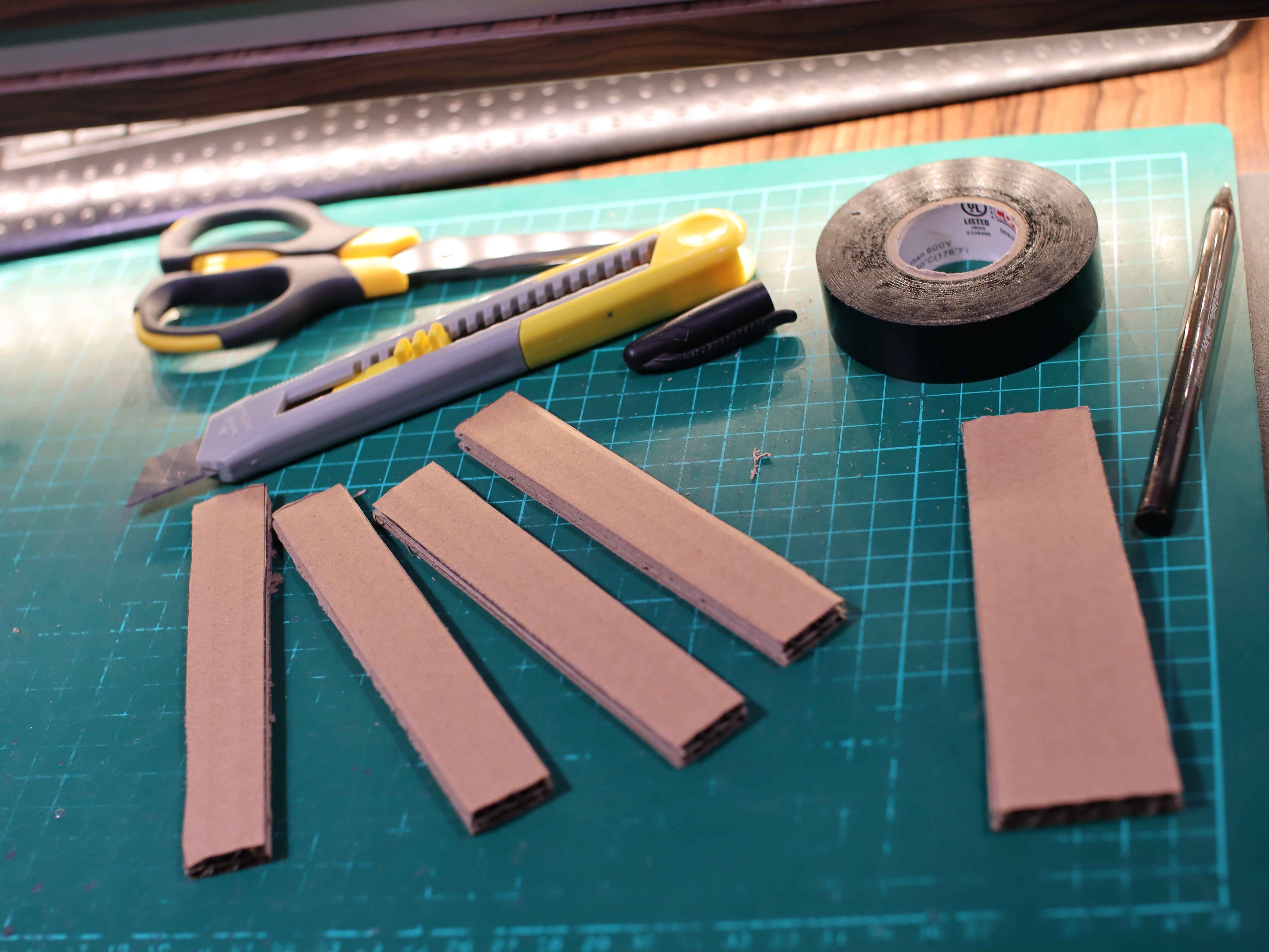 Airsoft battery elements cut out of cardboard. The knife, scissors, pen, electrical tape are on the green service mat.