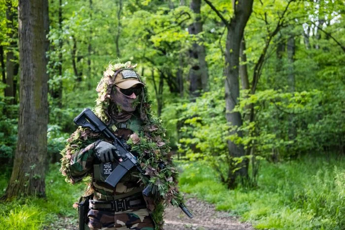 Airsoft player in camouflage clothing in forest