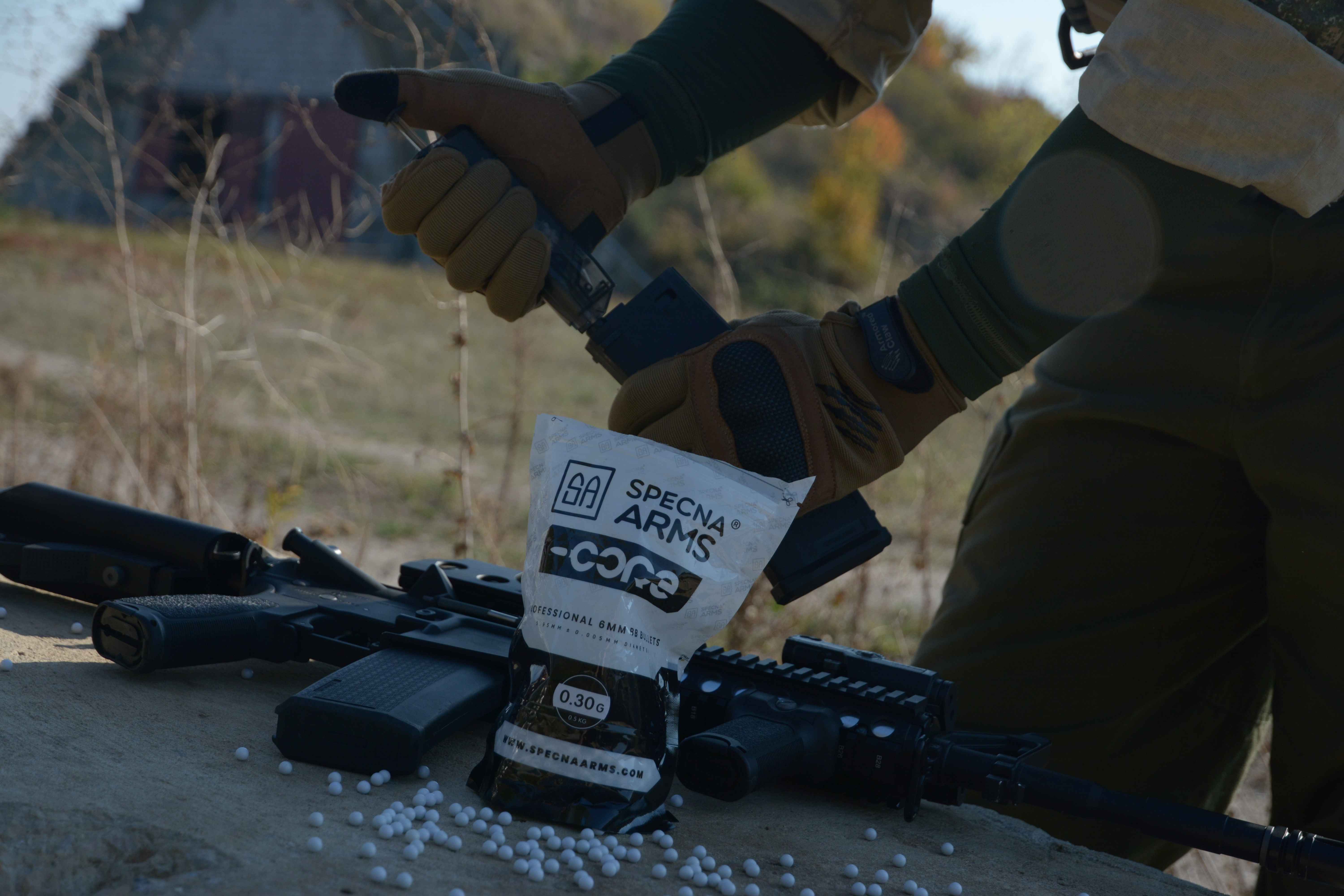 kulki specna arms core w opakowaniu na bloczku obok repliki airsoft; ładowanie kulek szybkoładowarką