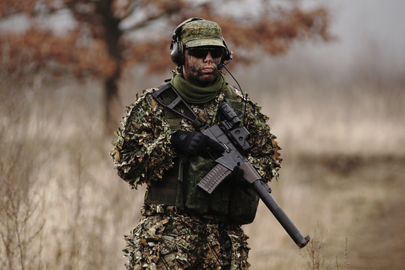 un homme en uniforme avec des tenues de camouflage et des lunettes de protection tient une réplique d'airsoft