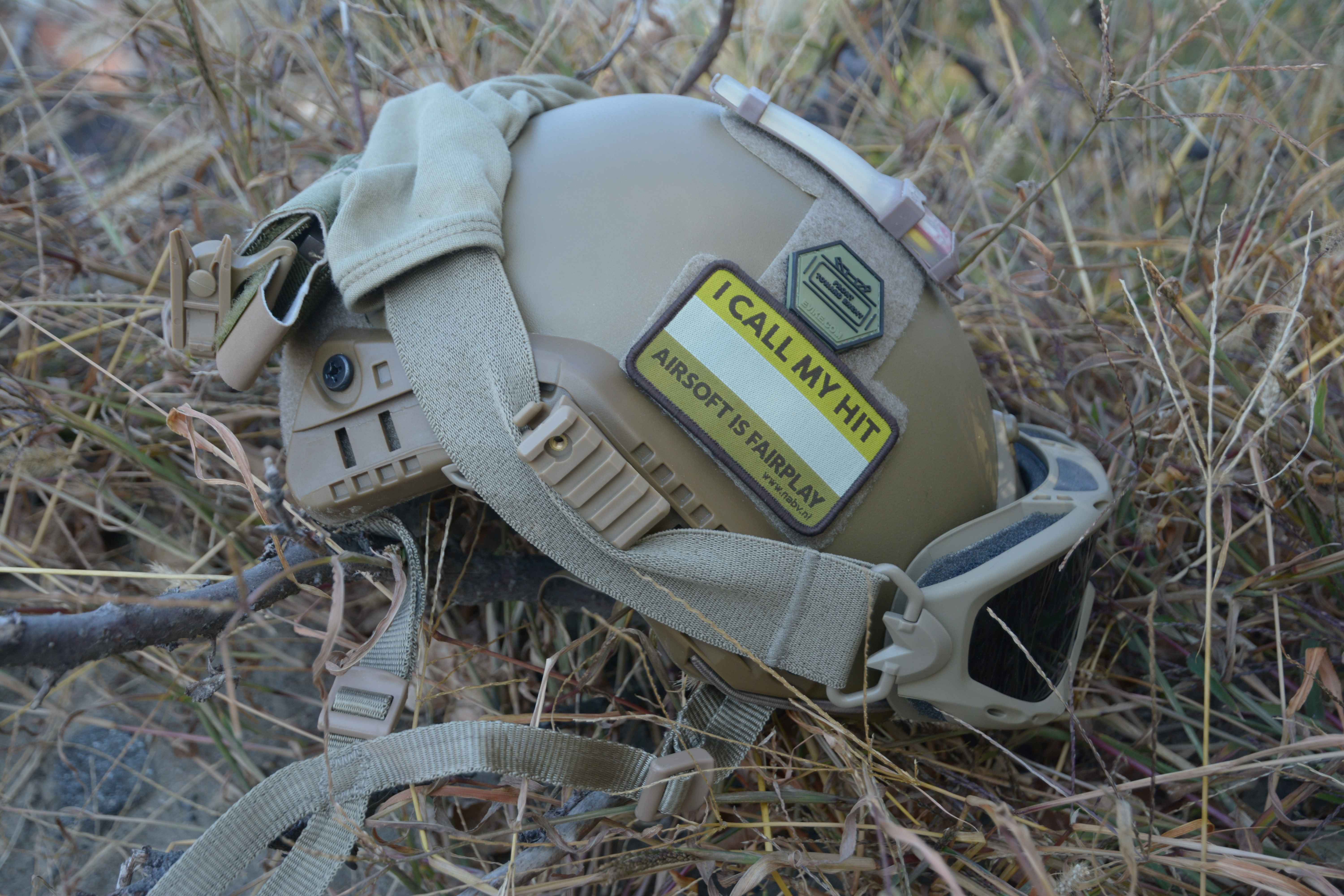 réplique d'un casque d'airsoft de couleur fauve avec patch ; pierre et herbe