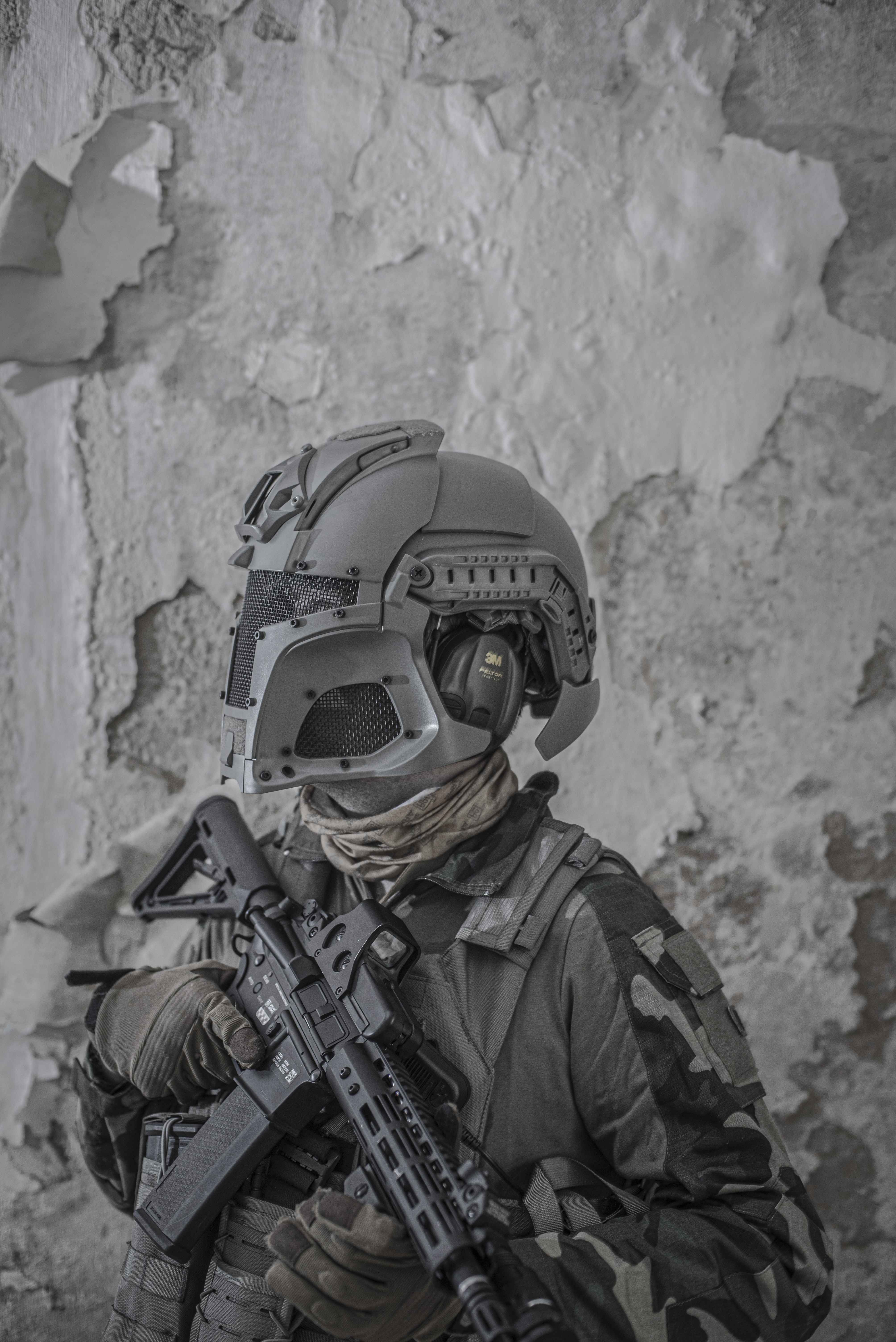 joueur d'airsoft portant un casque et un masque avec une réplique ; habillé en uniforme contre le mur