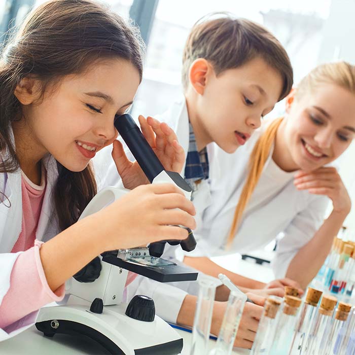 dziewczynka i chłopcy patrzą przez mikroskop